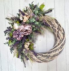 a wreath with purple flowers and greenery hanging on a white wooden wall in front of a door