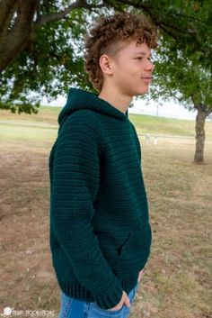 a young man standing under a tree wearing a green sweater