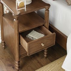 a night stand with an open drawer on the side and a bed in the background