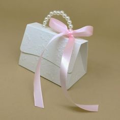 a small white box with a pink ribbon tied around it and a pearl beaded handle