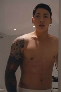 a shirtless man with tattoos standing in front of a bathroom mirror and looking at the camera