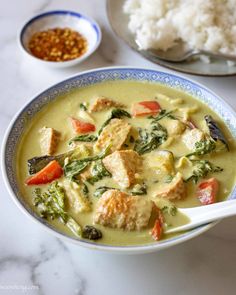 a bowl filled with soup next to rice and other foods on a table top,