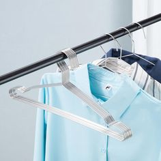 two shirts hanging on a rail in front of a window with clothes hangers attached to it