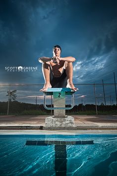 a man sitting on top of a diving board in a pool under a cloudy sky