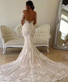 a woman is standing in front of a mirror wearing a wedding dress with an open back