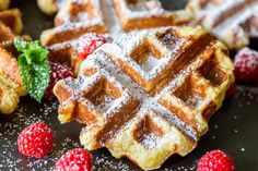 waffles with powdered sugar and raspberries on a black tablecloth