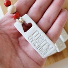 a hand holding a small white tag with red beads and a heart on it's end