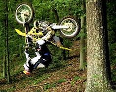 a person on a dirt bike doing a trick in the air over a forest trail