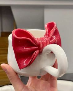 a hand holding a coffee cup with a red bow on it's handle and inside