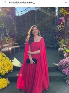 a woman in a red dress and cape standing on some steps with flowers behind her