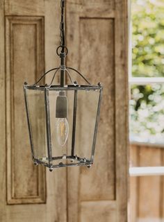 a light fixture hanging from the ceiling in front of a wooden door with an open window