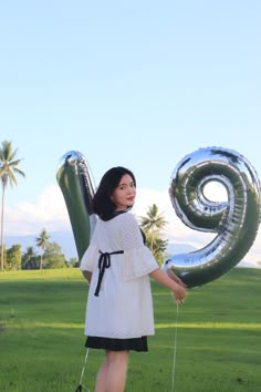 a woman in a white dress holding an air - filled number 9 balloon and walking