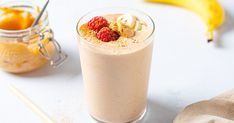 a smoothie in a glass topped with raspberries next to a banana and orange juice