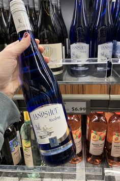 a person is holding a bottle of wine in front of some shelves with bottles on it