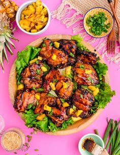 a pink table topped with plates and bowls filled with food next to pineapples