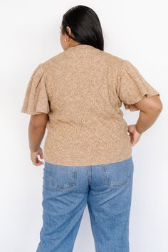 a woman standing with her back to the camera, wearing jeans and a tan sweater