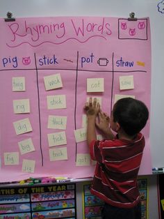 a young boy writing on a pink bulletin board with post - it notes attached to it