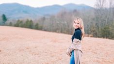 a woman standing in the middle of a field with mountains in the backgroud