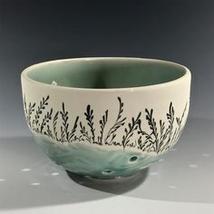 a white and green bowl with black designs on the rim, sitting on a table