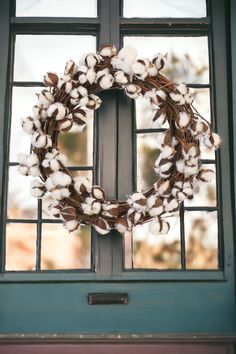 a wreath with cotton is hanging on the front door, next to an open window