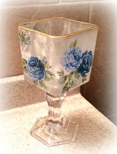 a glass vase sitting on top of a counter next to a tile wall with flowers painted on it