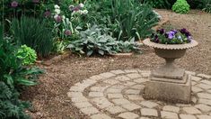 a garden filled with lots of plants and flowers next to a stone walkway in the middle of