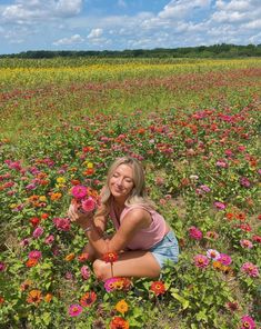 a woman kneeling in a field full of flowers holding onto some pink and yellow flowers