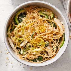 a bowl filled with noodles and vegetables next to a plate of broccoli on a table