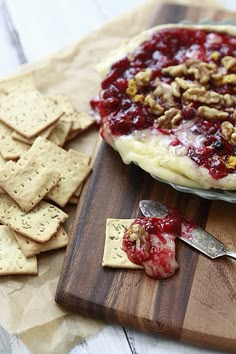 a wooden cutting board topped with crackers next to a bowl of cranberry sauce