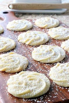 a wooden cutting board topped with cookies covered in powdered sugar