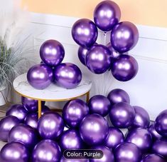 purple balloons are piled on top of each other near a table and potted plant