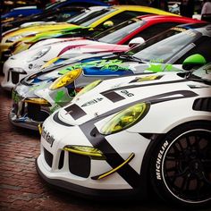 a row of colorful sports cars parked next to each other on a brick sidewalk in front of a building