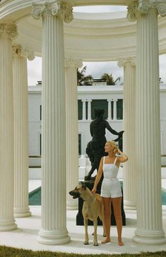 a woman standing next to a dog in front of a building with columns and statues