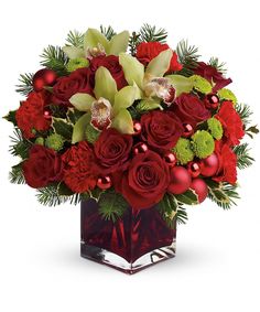 a christmas bouquet with red roses and green orchids in a square glass vase on a white background