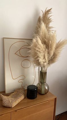 a vase with some dry grass in it next to a candle and an art piece