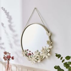 a mirror hanging on the wall next to a potted plant and vase with flowers