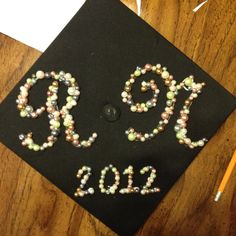 a graduation cap decorated with beads and writing on top of a wooden table next to a pencil