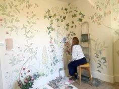 a woman sitting on a chair in front of a wall with flowers painted on it