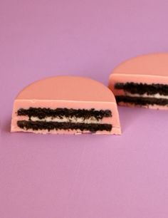 two pieces of cake sitting next to each other on a purple surface with pink and white frosting