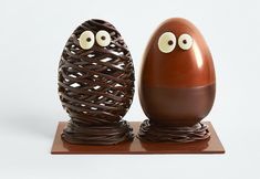 two chocolate eggs with googly eyes sitting side by side on a wooden stand, one is brown and the other is white