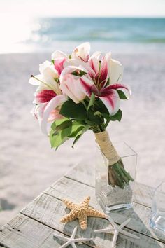 a bouquet of flowers sitting on top of a wooden table next to the ocean and starfish