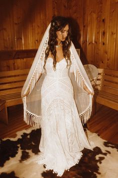 a woman in a white dress and veil standing on a cowhide rug next to wooden benches