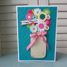 a handmade card with flowers in a mason jar on top of a blue table