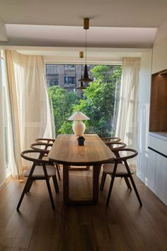 a dining room table with chairs and a vase on it in front of an open window