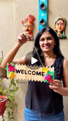 a woman standing in front of a welcome sign with flowers and masks on the wall behind her