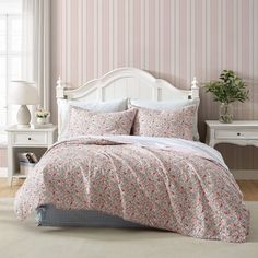 a bedroom with pink and white striped wallpaper, bed linens and a wooden headboard