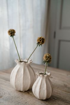 two white vases sitting on top of a wooden table next to each other with yellow flowers in them