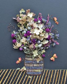 a vase filled with purple and white flowers on top of a wooden table next to a wall