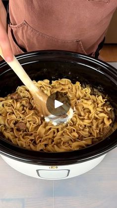 a person stirring noodles in a slow cooker