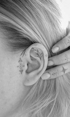 a woman with tattoos on her ear and behind the ear is a small flower tattoo